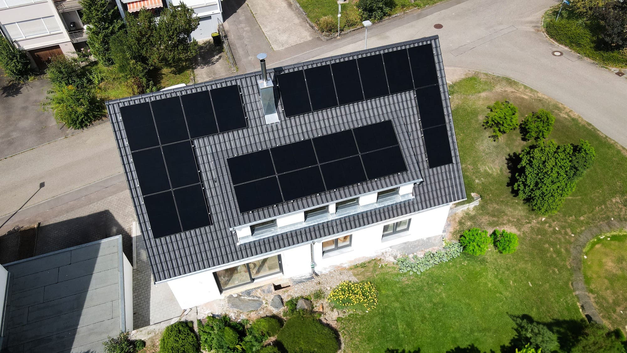 Luftaufnahme eines Einfamilienhauses mit großflächiger Photovoltaikanlage auf dem Dach und schwarzen Solarmodulen